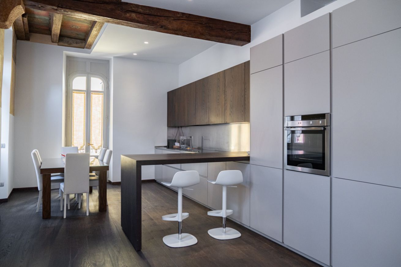 Une cuisine moderne avec des meubles blancs, un plan de travail foncé et un four encastré. On y trouve également un coin repas avec une table et des chaises.