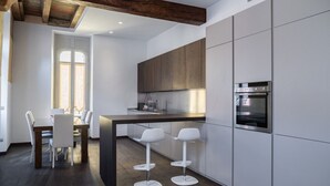 A modern kitchen with white cabinetry, a dark countertop, and a built-in oven. There is a dining area with a table and chairs. - Majestic Mazzini Residence with 3 bedrooms and 3 bathrooms (Verona)