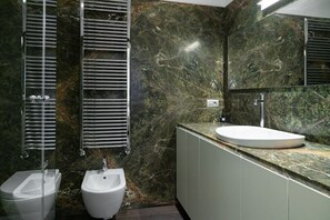 A modern bathroom with a marble wall, a sink, and two urinals.