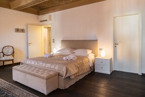 A spacious bedroom with a large bed, bedside lamps, a chair, and a nightstand.