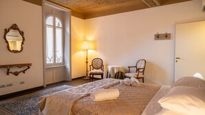 A hotel room with a large bed, a sitting area with two chairs, a small table, a mirror, and a window with curtains. - Majestic Mazzini Residence with 3 bedrooms and 3 bathrooms (Verona)