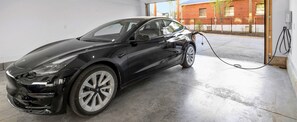 A black car parked inside a garage with a charging cable connected to an external charging station.