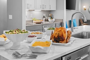 Una cocina moderna con un pavo grande como plato principal, diferentes acompañamientos y un lavamanos de acero inoxidable.
