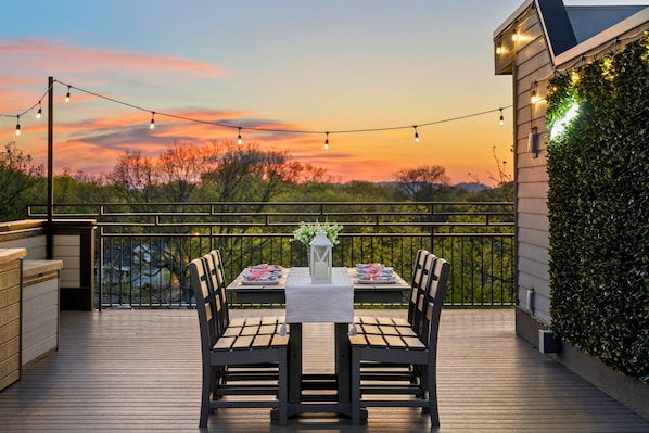 A wooden deck with a table set for two, surrounded by chairs, and string lights above.