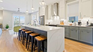 Cocina moderna con una isla grande, taburetes de bar y electrodomésticos de acero inoxidable.