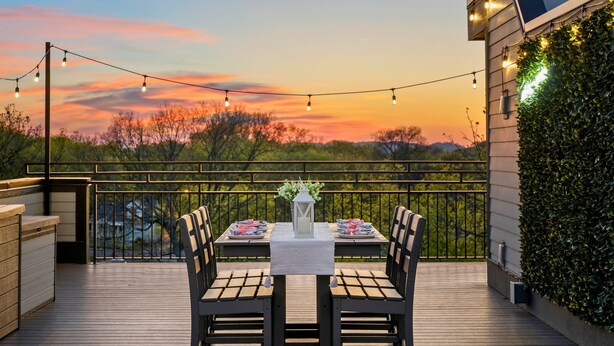 Una terraza al aire libre con una mesa preparada para dos, luces colgantes y vistas al atardecer.