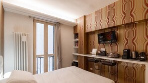 Una habitación de hotel con cama, televisión, repisa con artículos de aseo y ventana con cortinas.
