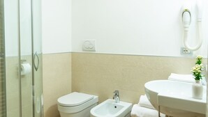 Un baño con mampara de vidrio, inodoro, bidé, lavabo y toallero.