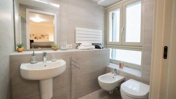 Ein modernes Badezimmer mit einem großen Waschbecken, einem Bidet und einer Toilette, einem Spiegel und einem Fenster für natürliches Licht.