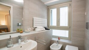 Un baño moderno con lavamanos, bidé, inodoro, una ventana y un espejo.