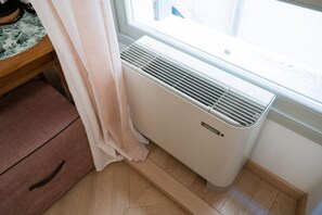 Una habitación con ventana, radiador, suelo de madera y una silla rosa.