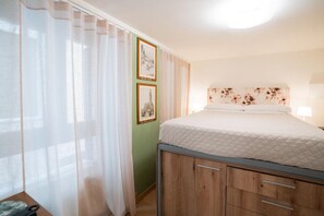 A bedroom with a bed, curtains, a headboard with floral design, and two framed pictures on the wall. - Cozy room in the heart of the city  (Verona)