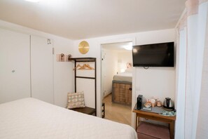 Un dormitorio con cama, televisión, armario, mesita de noche con hervidor y una pequeña mesa con cafetera.