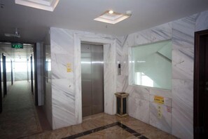 Un pasillo con suelo de mármol, un ascensor y una puerta de cristal.