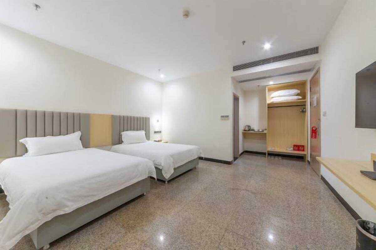A hotel room with two beds, a wooden wardrobe, a TV, and a bathroom visible through an open door.