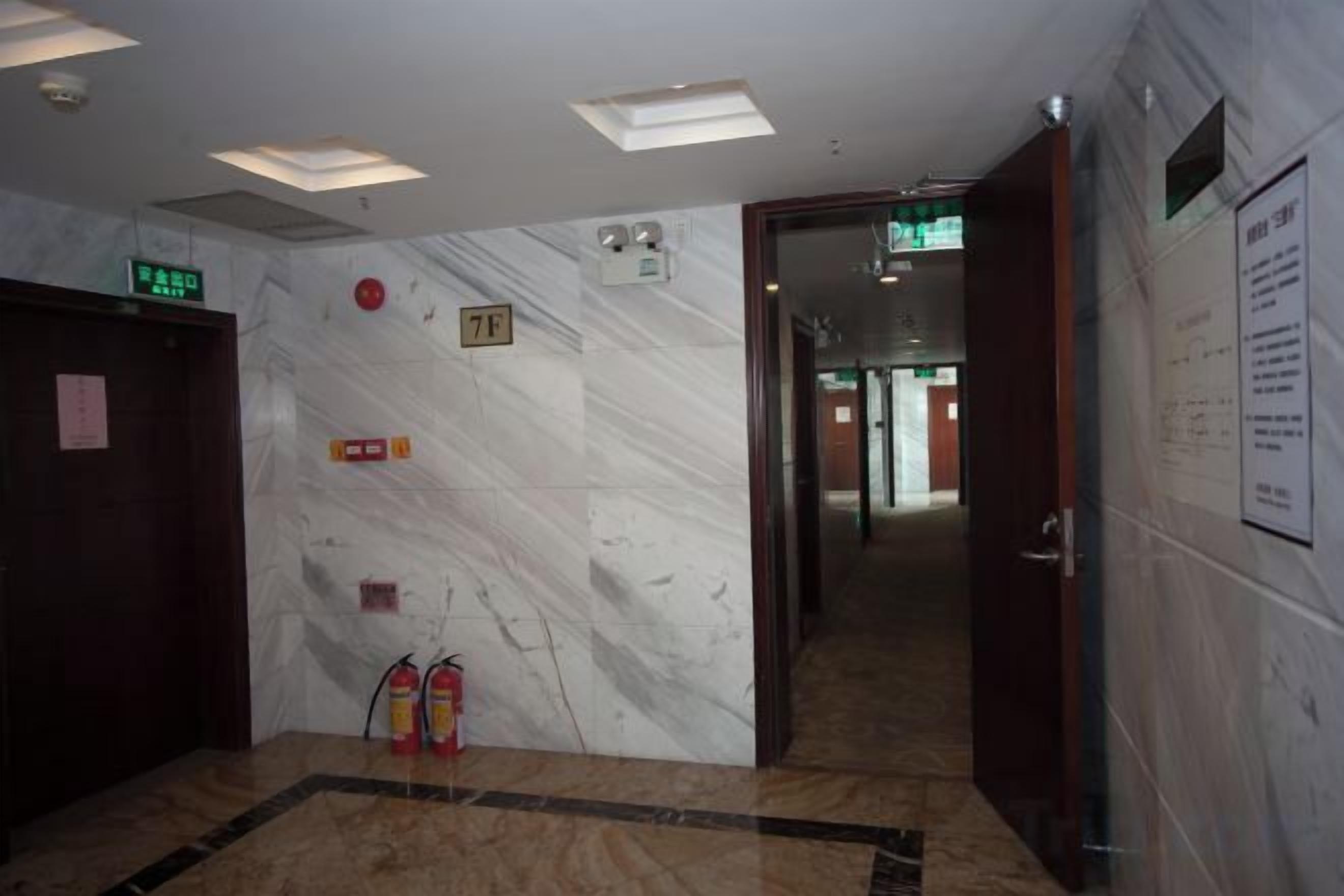 A hotel lobby with a marble wall, a fire extinguisher, and an emergency exit sign.