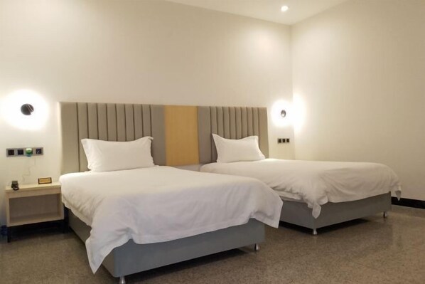 Habitación de hotel con dos camas, cabecera con líneas verticales, lámparas de noche y una mesita de noche con un reloj.