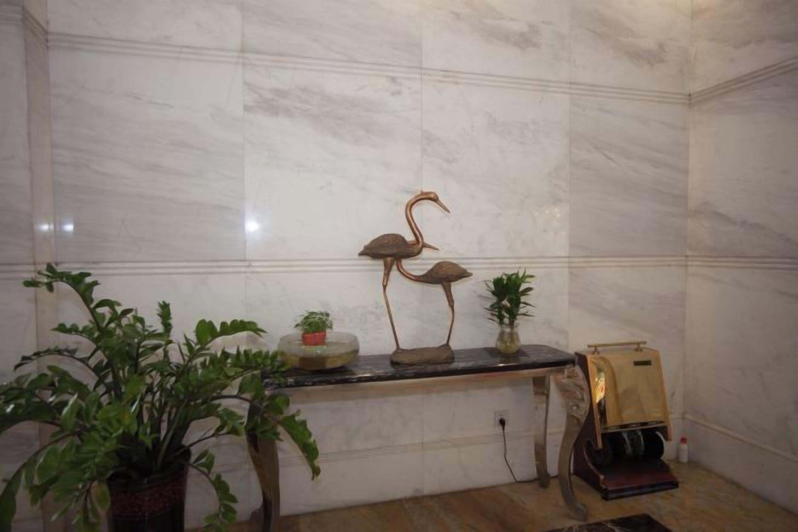 Un mur de marbre agrémenté d’un banc en bois, d’une sculpture en métal et de plantes en pot.