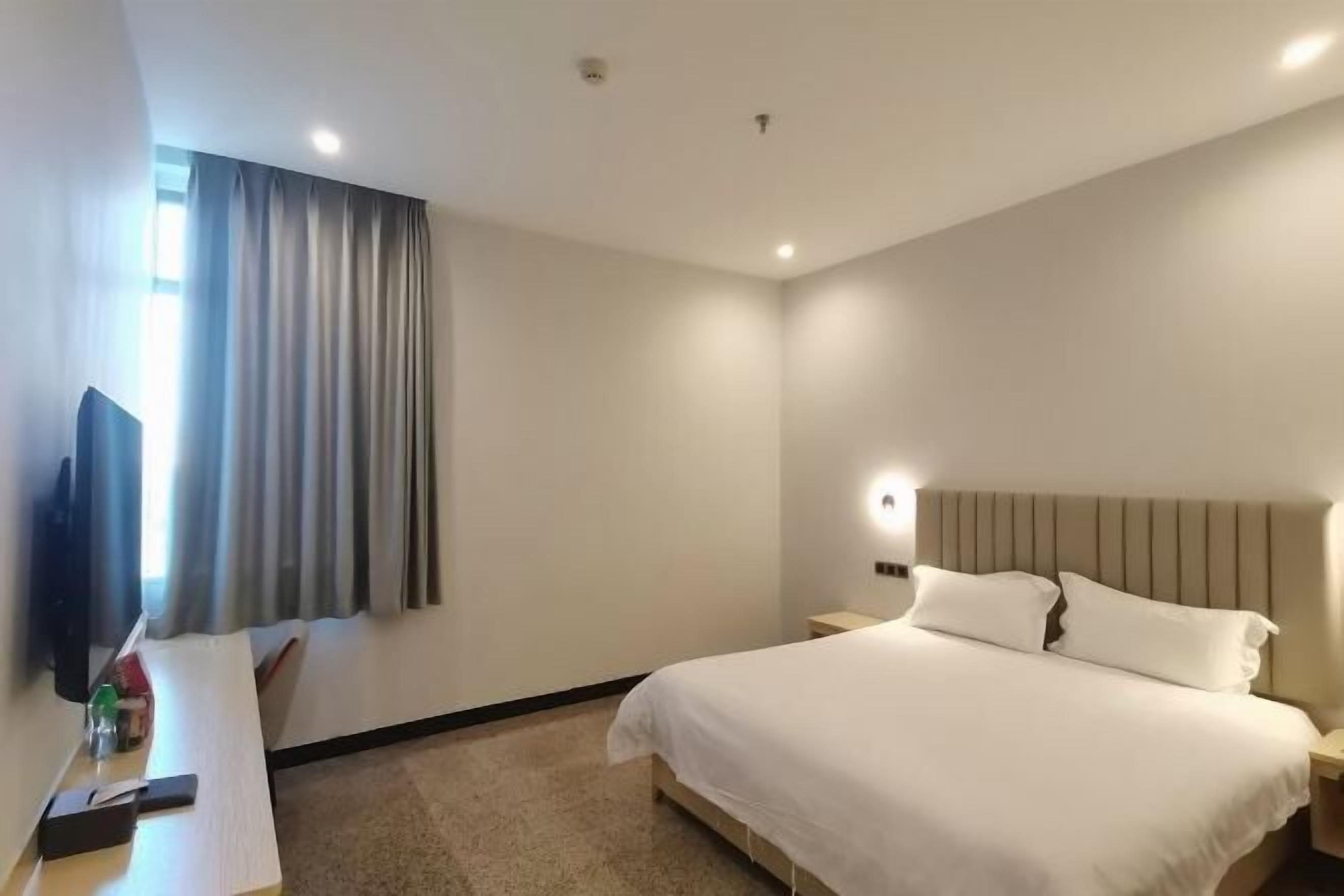 A hotel room with a bed, a TV, a desk, and a window with curtains.
