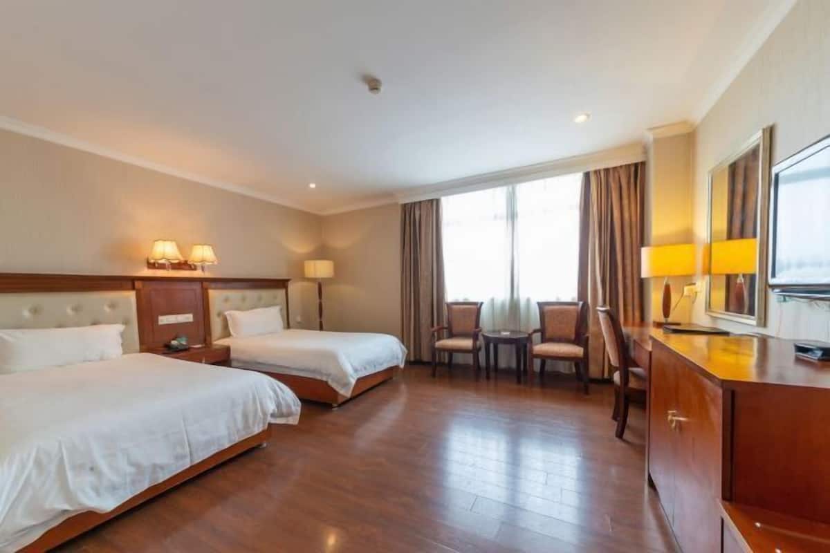A hotel room with two beds, a desk, a chair, a small table, and a large window with curtains.