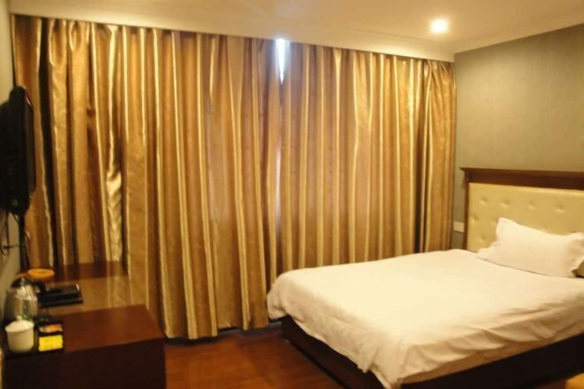 A hotel room with a bed, curtains, a bedside table, and a wall-mounted lamp.