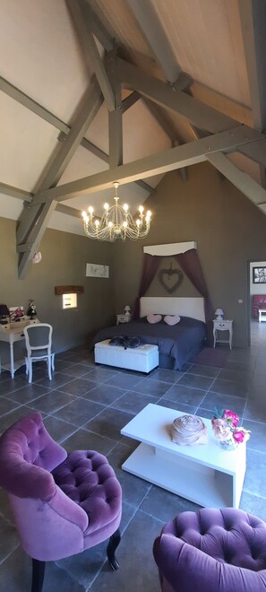 Ruime loft slaapkamer met een schuine kap, een groot bed, een bureau en paarse fauteuils.