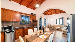A modern kitchen with wooden cabinets, a microwave, and a dining area with a table set for four. - Du Lac Villas 2 Private Pools (Kavallos)