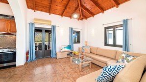 A spacious living area with a wooden ceiling, a kitchen with a stove, and a dining area with a table and chairs. - Du Lac Villas 2 Private Pools (Kavallos)