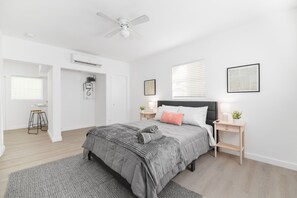 Quarto moderno com cama, mesas de cabeceira, ventilador de teto e janela com persianas.