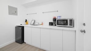 A compact kitchen with white cabinets, a black refrigerator, a microwave, and a coffee maker on the countertop. - Miami in Style Near Wynwood - We Host (Miami)