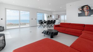 A spacious living room with a red sofa, a dining area with a table and chairs, and a large painting on the wall.
