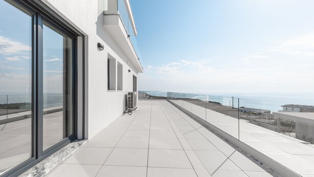 A modern building with large windows and a balcony overlooking a coastal view.