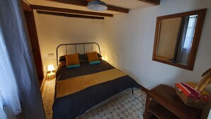 Ein Schlafzimmer mit einem Bett, einem Holz-Kopfbrett, einem Nachttisch, einer Lampe, einem Spiegel und einem Boden mit geometrischem Muster.