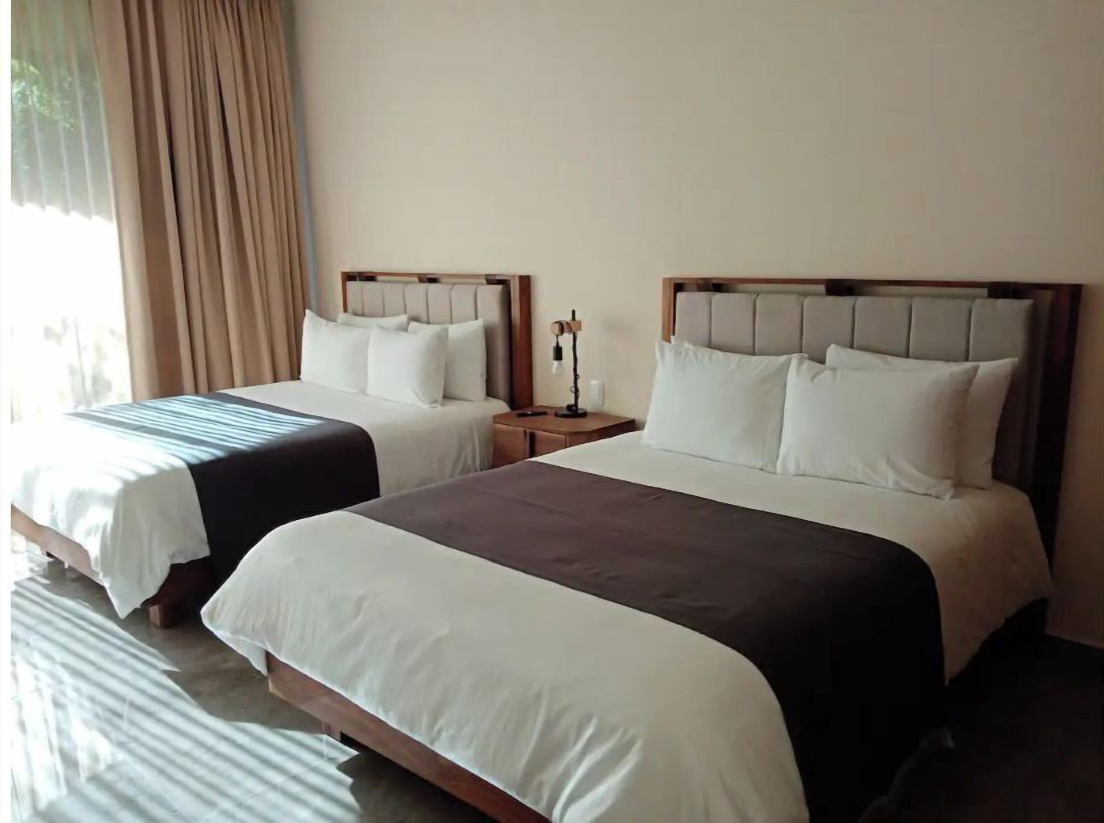 Two double beds with headboards, a bedside table with a lamp, and a window with curtains.