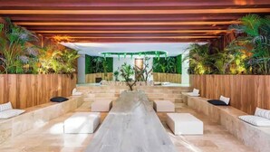 A modern outdoor lounge area with tiered seating, wooden accents, and lush greenery. - Wonderful studio in Menesse Condominium (Tulum)