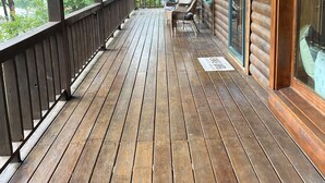 Una terraza de madera con barandilla, un árbol grande y dos sillas de mimbre.