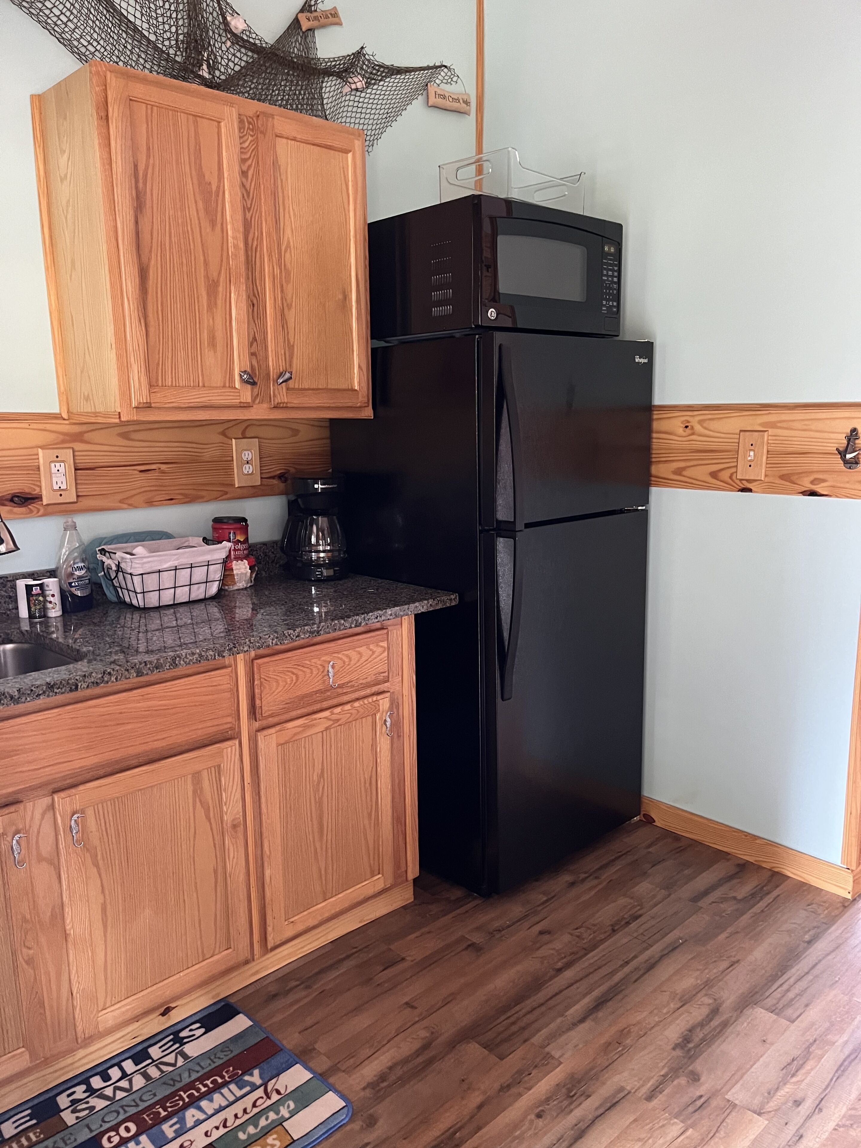 A kitchen with wooden cabinets, a black refrigerator, and a granite countertop.
