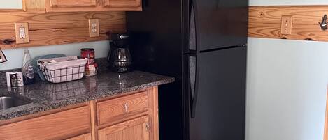 A kitchen with wooden cabinets, a black refrigerator, and a granite countertop.