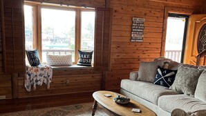 Interior acogedor de una cabaña con techo de madera, un sofá, una mesa de centro y un ventanal con vistas a un lago.