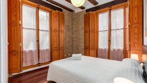 A bedroom with a large bed, wooden wardrobe, and a stone wall.