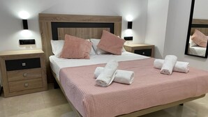 A neatly made bed with pink bedding, two bedside tables, and a mirror on the wall.