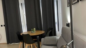 A modern living room with a grey sofa, a wooden dining table with black chairs, and a small cactus decoration.
