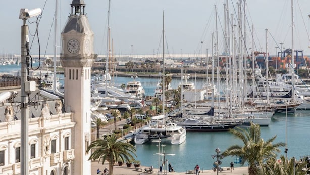 A marina with multiple yachts docked, a clock tower, and a building with classical architecture.