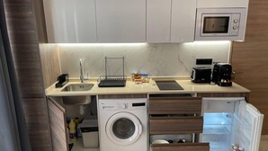 Een kleine keuken met een ingebouwde wasmachine, een magnetron en een koffiezetapparaat.