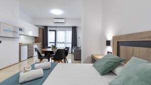 Une chambre d’hôtel moderne équipée d’un lit, d’un bureau, d’une chaise, d’une petite kitchenette et d’un coin repas.