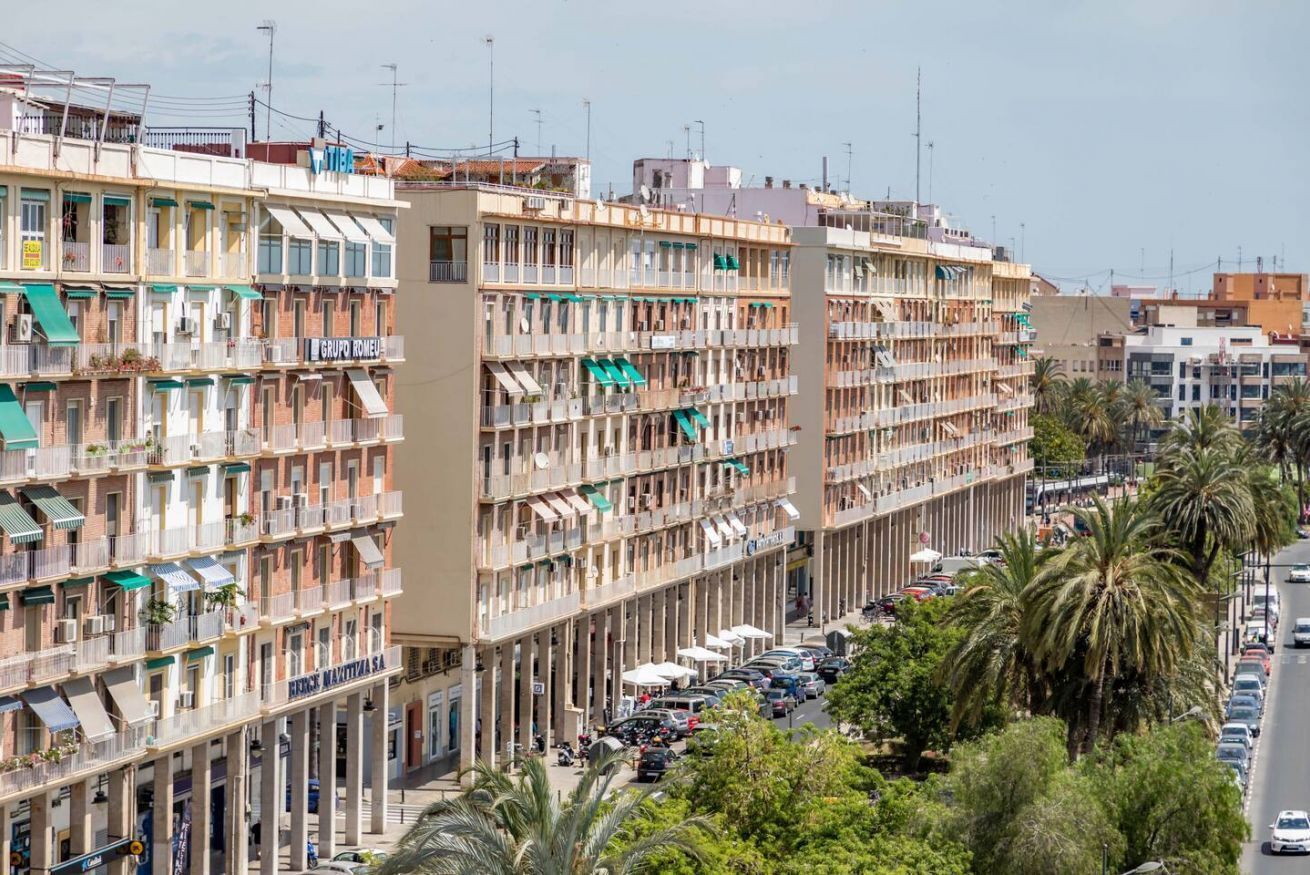 A multi-story building with balconies, a street in front, and parked cars.