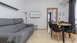 Una sala de estar moderna con un sofá gris, una mesa de comedor con sillas negras y un cartel enmarcado en la pared.