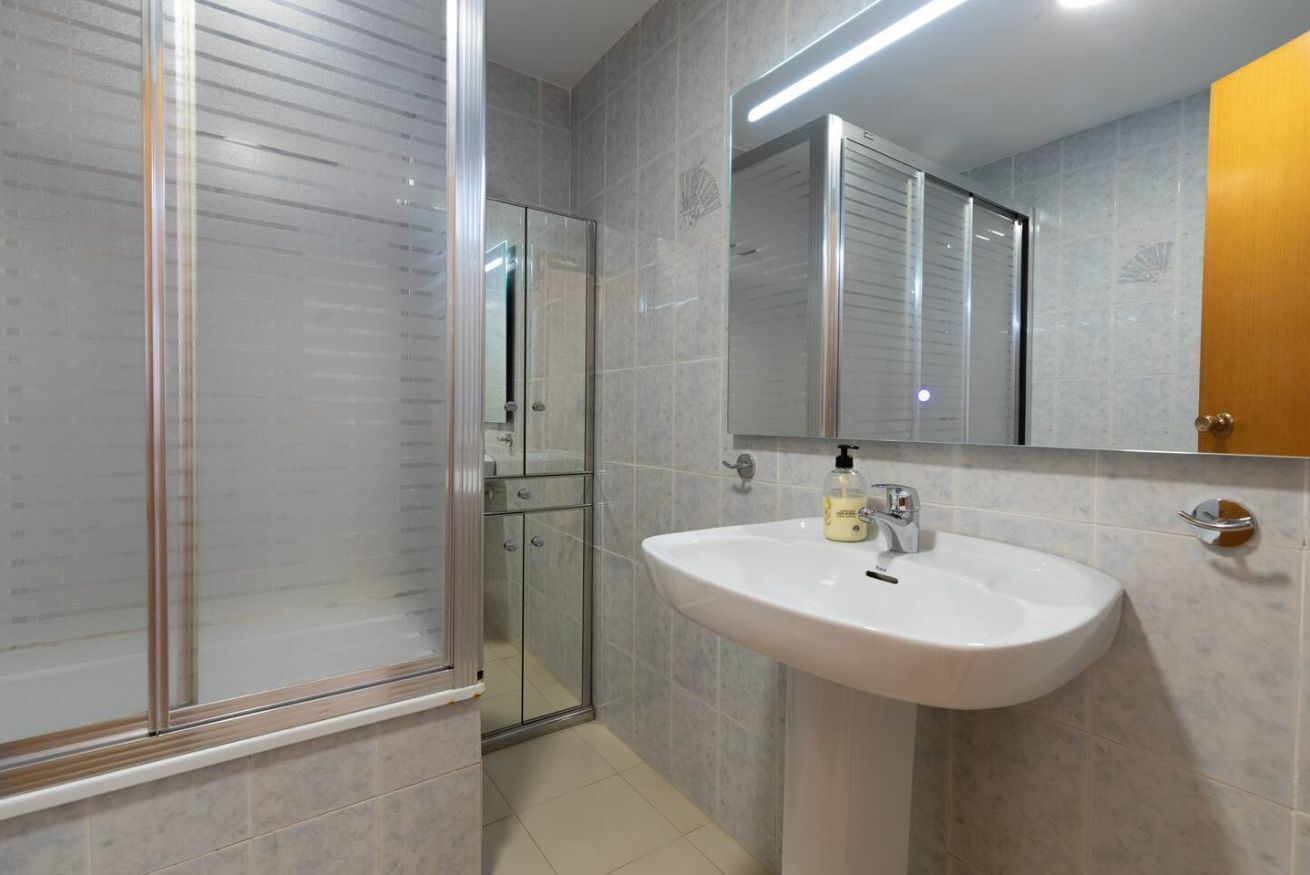 Un baño con cabina de ducha de vidrio, un lavabo blanco con dispensador de jabón y un espejo sobre el lavabo.
