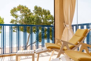 Un balcon avec vue sur la mer et les arbres, comprenant deux chaises longues et une petite table.