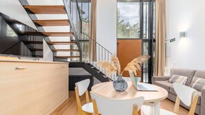 A modern living room with a round wooden table, white chairs, a sofa, and a staircase with wooden steps. - Alameda suites loft 1. (Valencia / València)